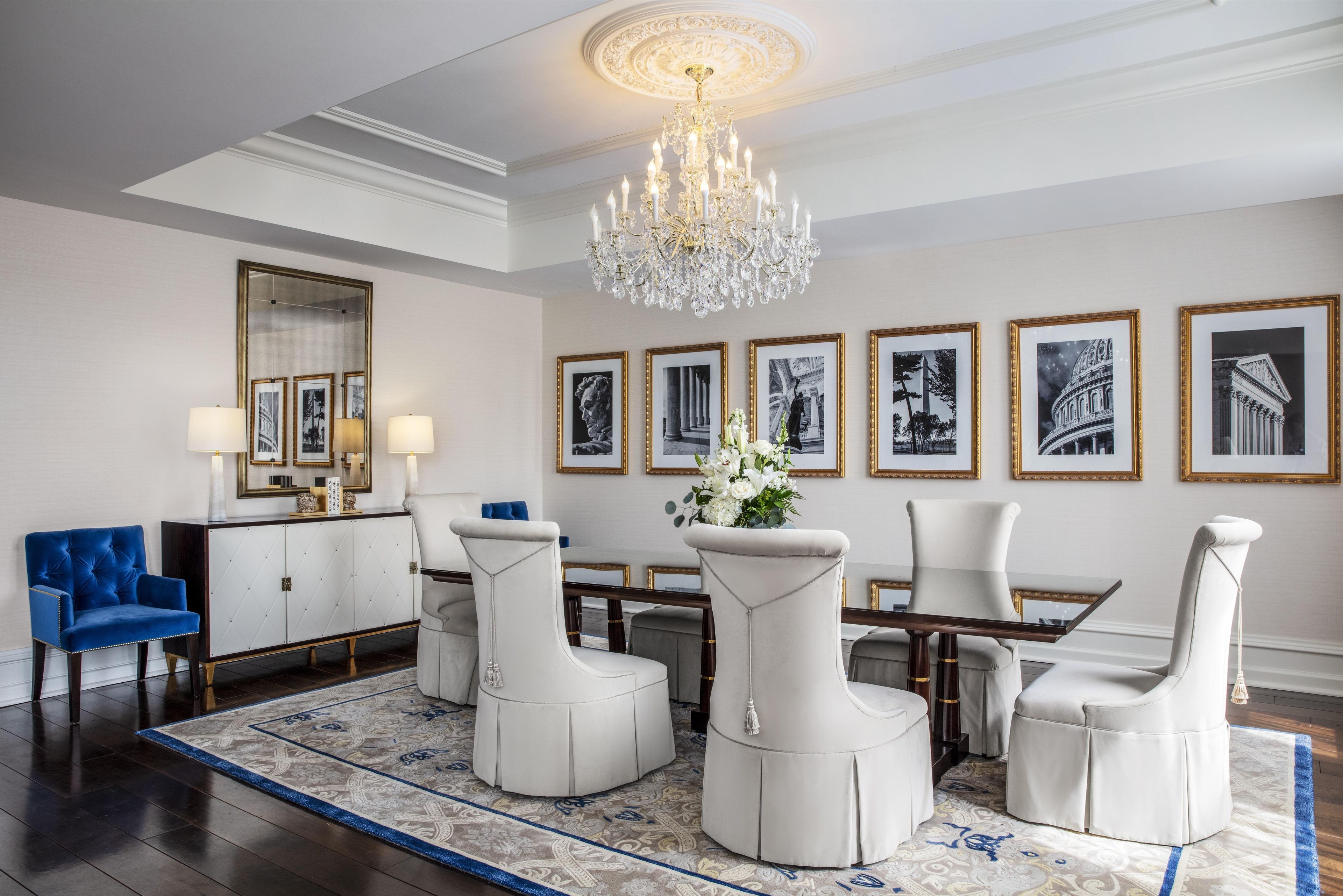 A formal dining room with a chandelier, framed artwork, and a blue armchair.