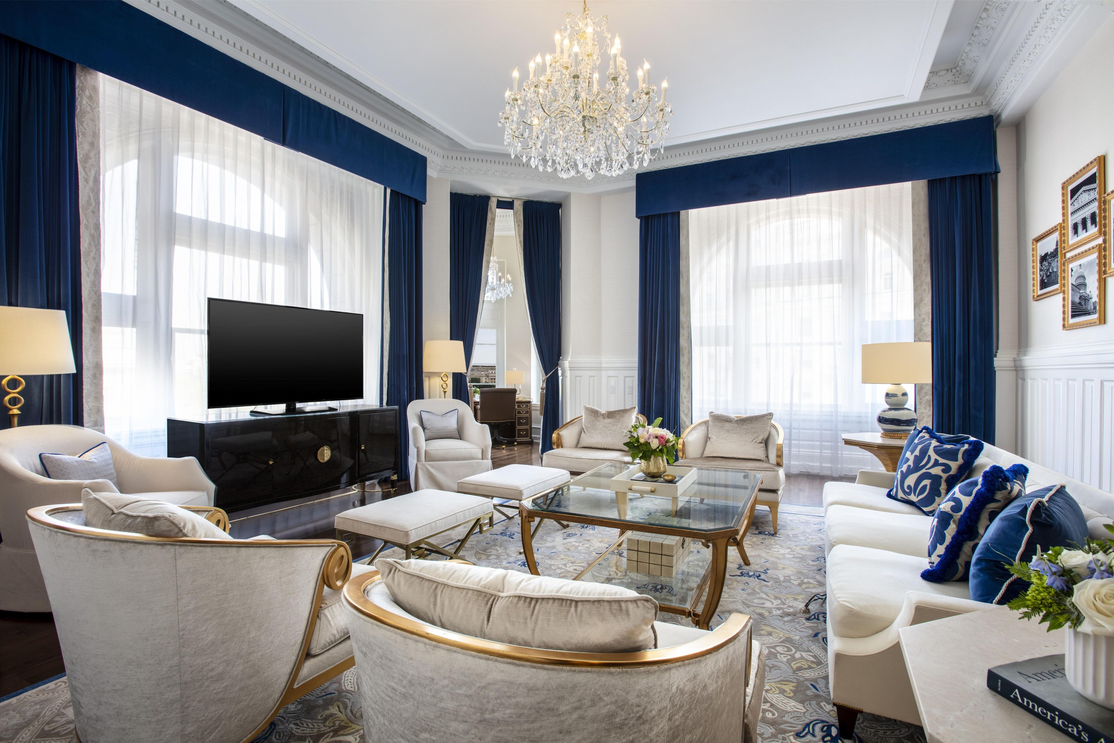 A luxurious living room with a large chandelier, a flat-screen TV, and elegant furniture.