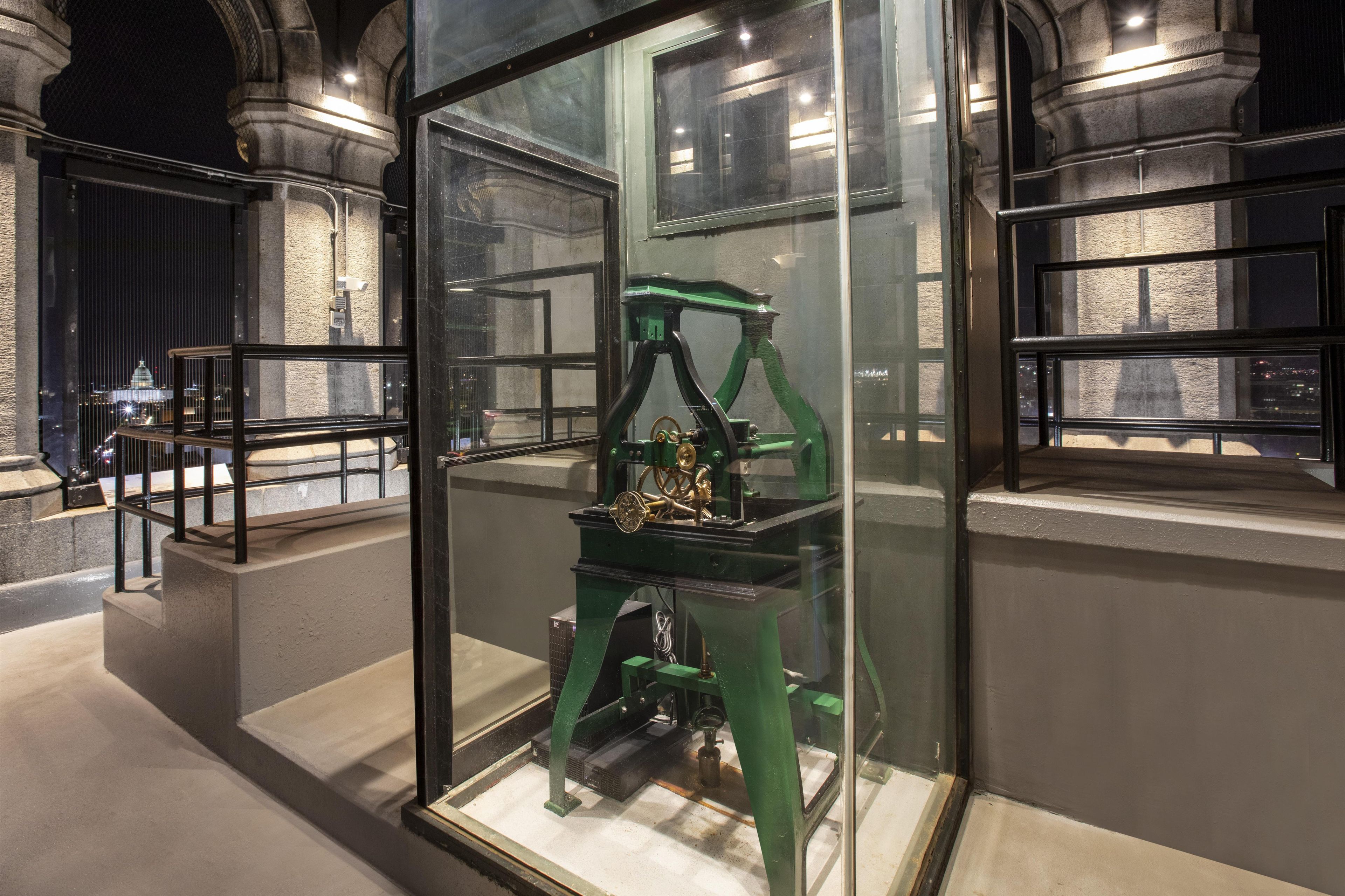 Una exhibición de museo con un dispositivo mecánico dentro de una vitrina, rodeada de arquitectura de piedra.