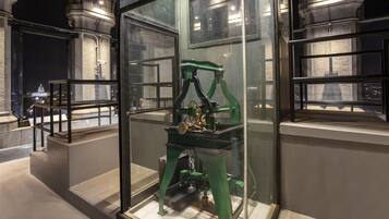 Una exhibición de museo con un dispositivo mecánico dentro de una vitrina, rodeada de arquitectura de piedra.