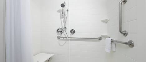 A modern bathroom with white tiles, a shower with a handheld showerhead, grab bars, and a towel rack.
