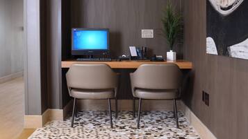 A reception desk with a computer, two chairs, a plant, and a sign with contact information.