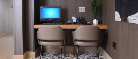 A reception desk with a computer, two chairs, a plant, and a sign with contact information.