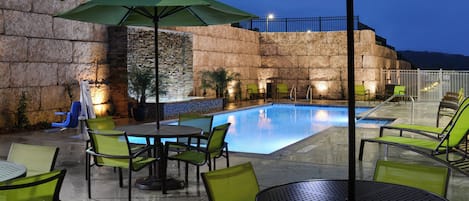 An outdoor pool area with stone walls, green chairs, and umbrellas.