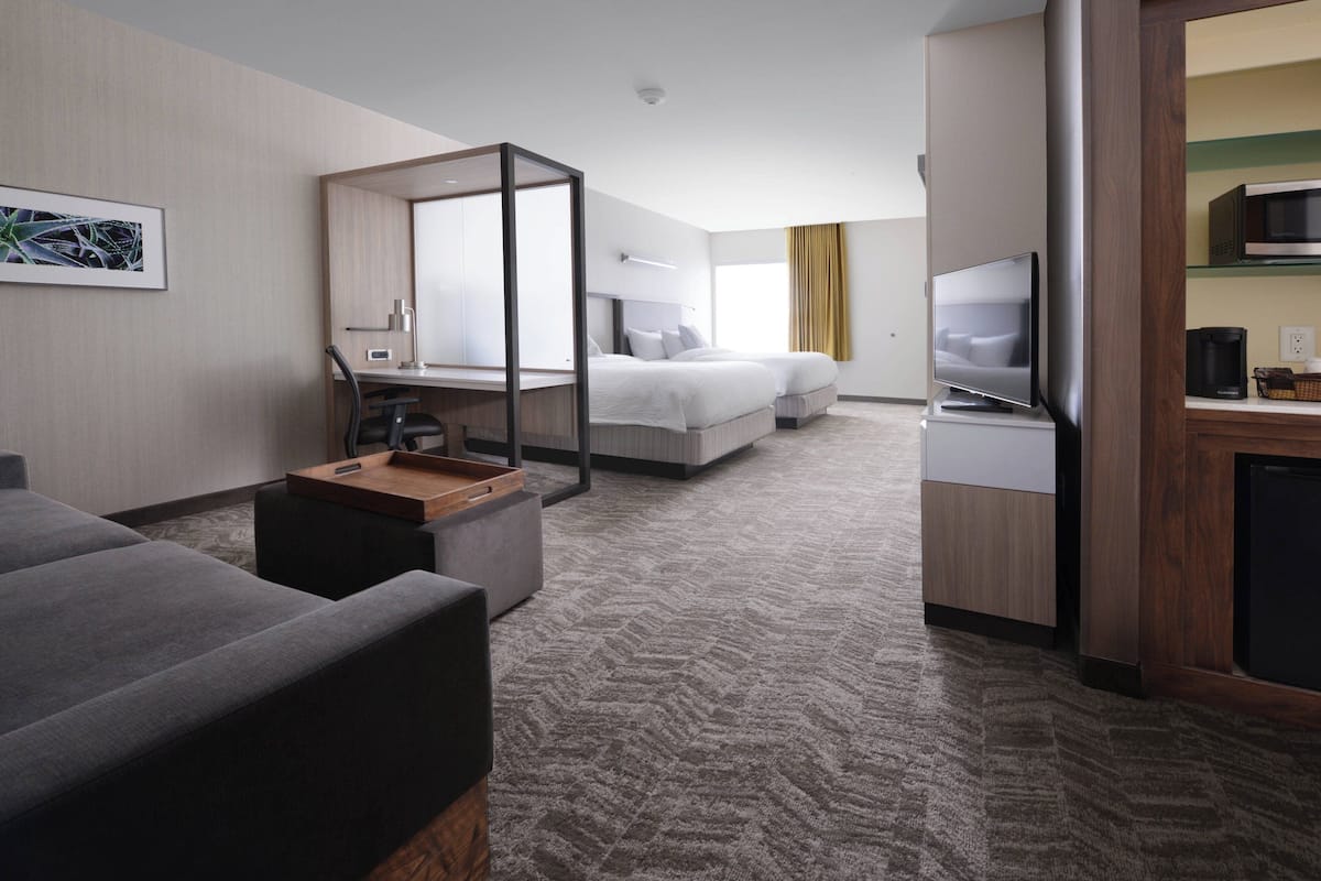 Ein modernes Hotelzimmer mit einem großen Bett, einem Schreibtisch mit Stuhl, einem Fernseher und einer Mikrowelle.