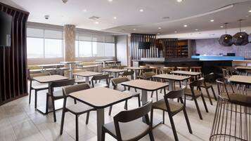 Un ristorante moderno con diversi tavoli e sedie, un'area bar e ampie finestre che permettono l'ingresso di luce naturale.