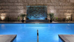 Una piscina con un muro de piedra de fondo, una fuente de agua y plantas en macetas.