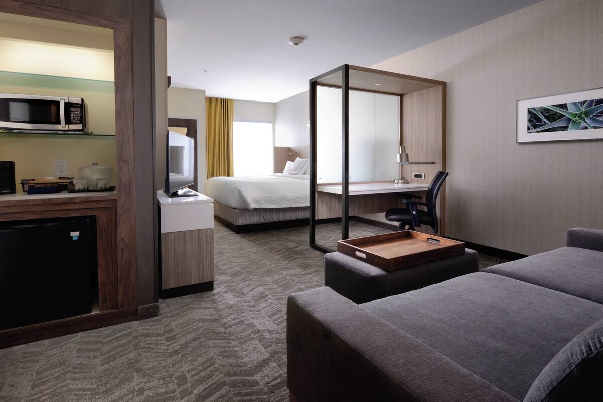 Ein Hotelzimmer mit einem Bett, einem Schreibtisch, einem Sessel, einer Mikrowelle, einem Kühlschrank und einem Fernseher.