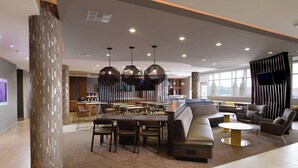 Un área de lounge moderna con una disposición central de asientos, un bar y una pantalla de televisión.