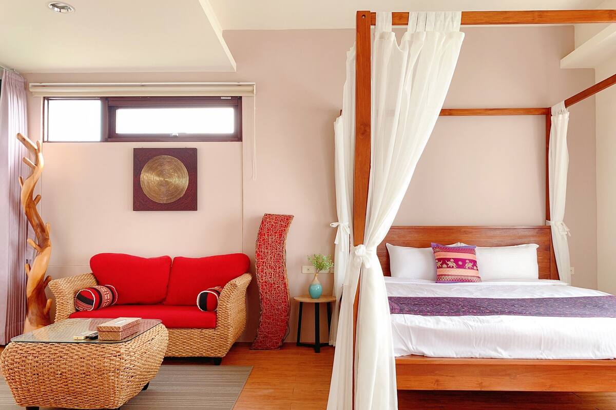 A bedroom with a four-poster bed, a red sofa, a wicker coffee table, and a wooden headboard.