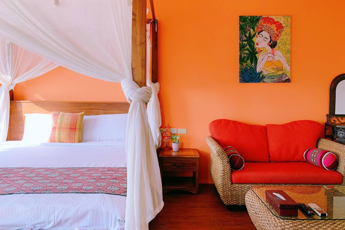 A room with a bed, a red sofa, a small table, and a painting on the wall.
