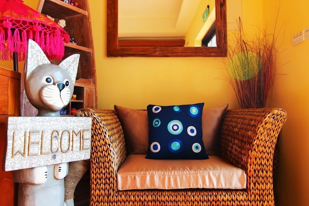 A wicker sofa with a cushion, a 'WELCOME' sign, and a decorative cat statue.