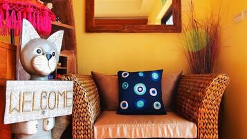 A wicker sofa with a cushion, a 'WELCOME' sign, and a decorative cat statue.