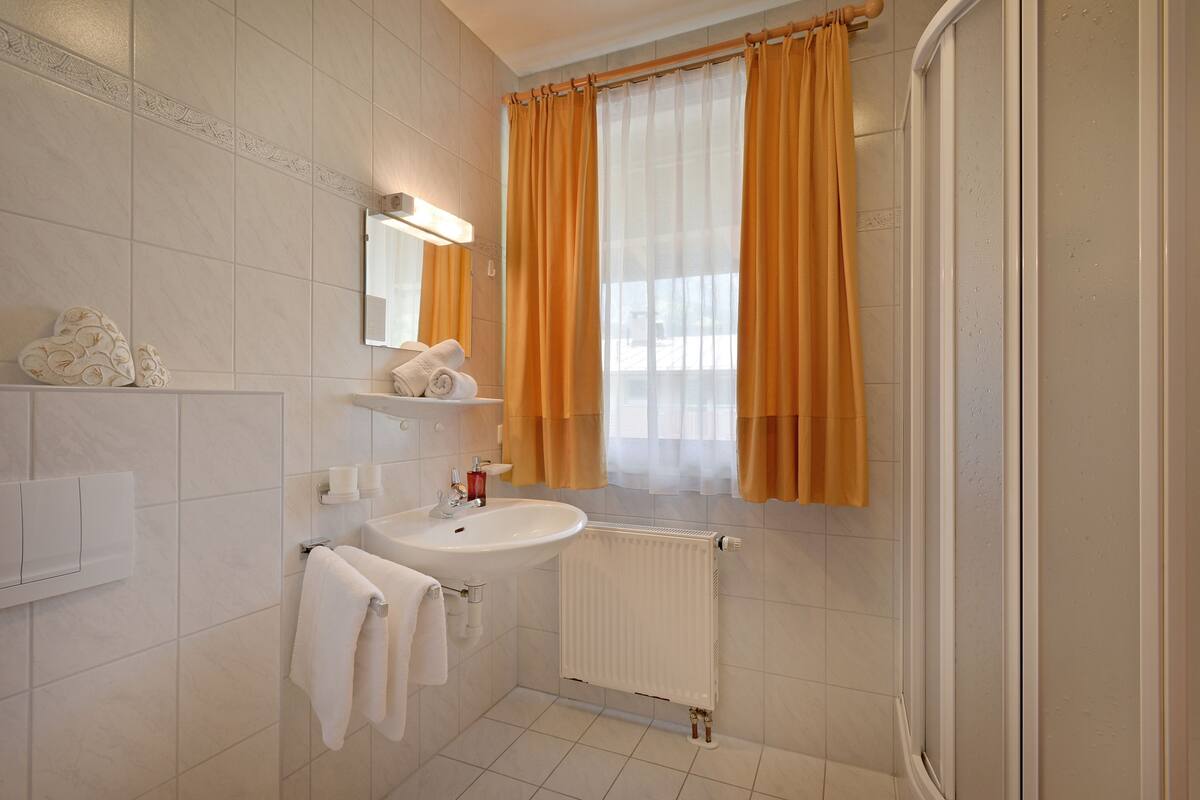 Une salle de bain équipée d’un lavabo, d’un miroir, d’un porte-serviettes et d’une fenêtre avec des rideaux.