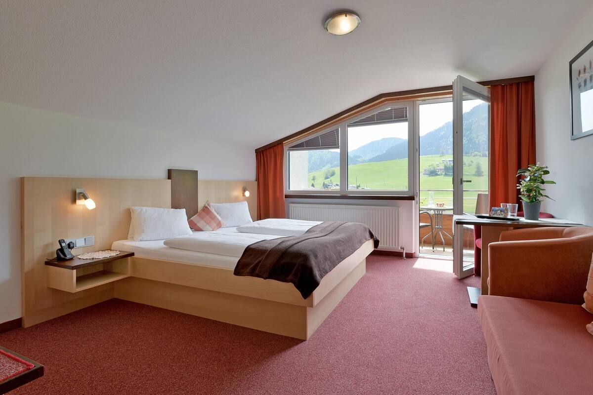 Une chambre d’hôtel avec un lit, un bureau, une chaise, une fenêtre donnant sur la campagne et une plante.