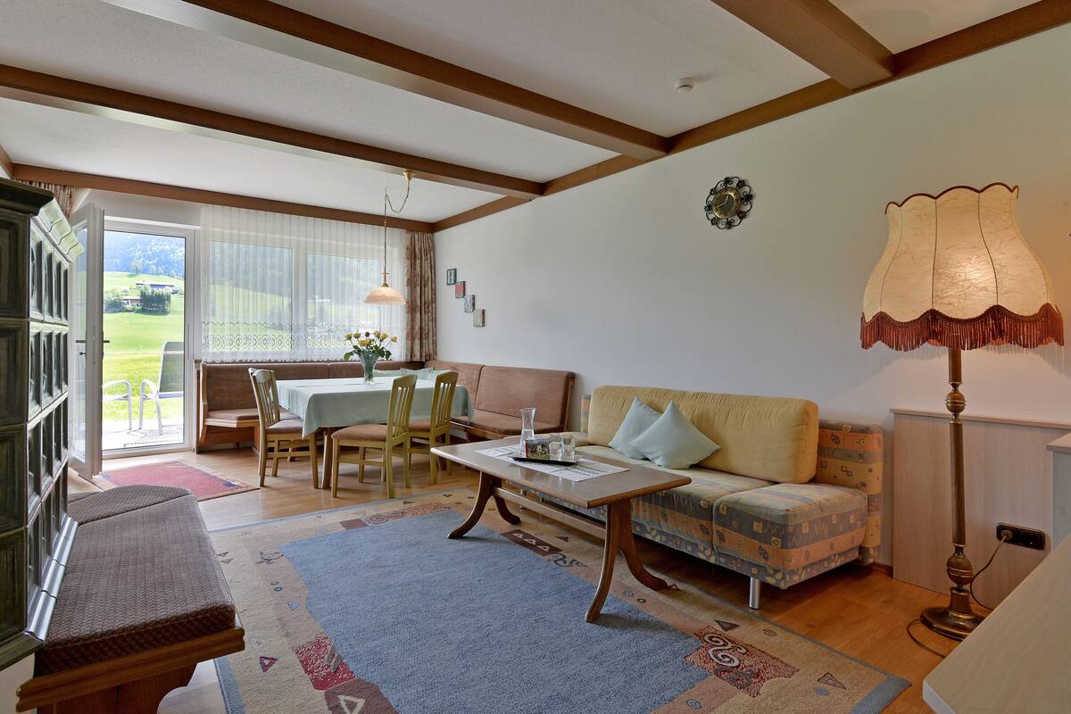 Un salon confortable avec un canapé, une table et un banc. Une fenêtre offre une vue sur l’extérieur.