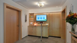 Et hotellets receptionområde med en træreception, et tv der viser en skærm, og en vase med blomster.