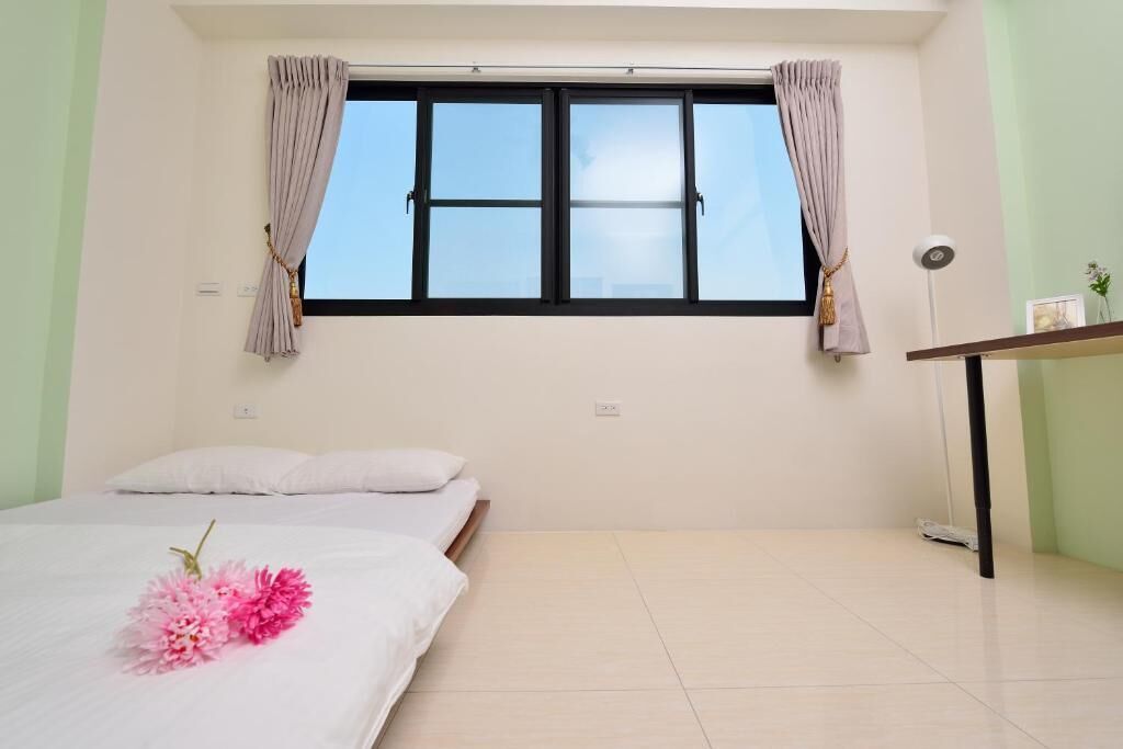 A room with a bed, a window with curtains, a bedside table, and a floor lamp.