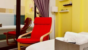 A hotel room with a bed, a red chair, a small table, an air conditioning unit, and a window with curtains. - STSP Guest House (Tainan)