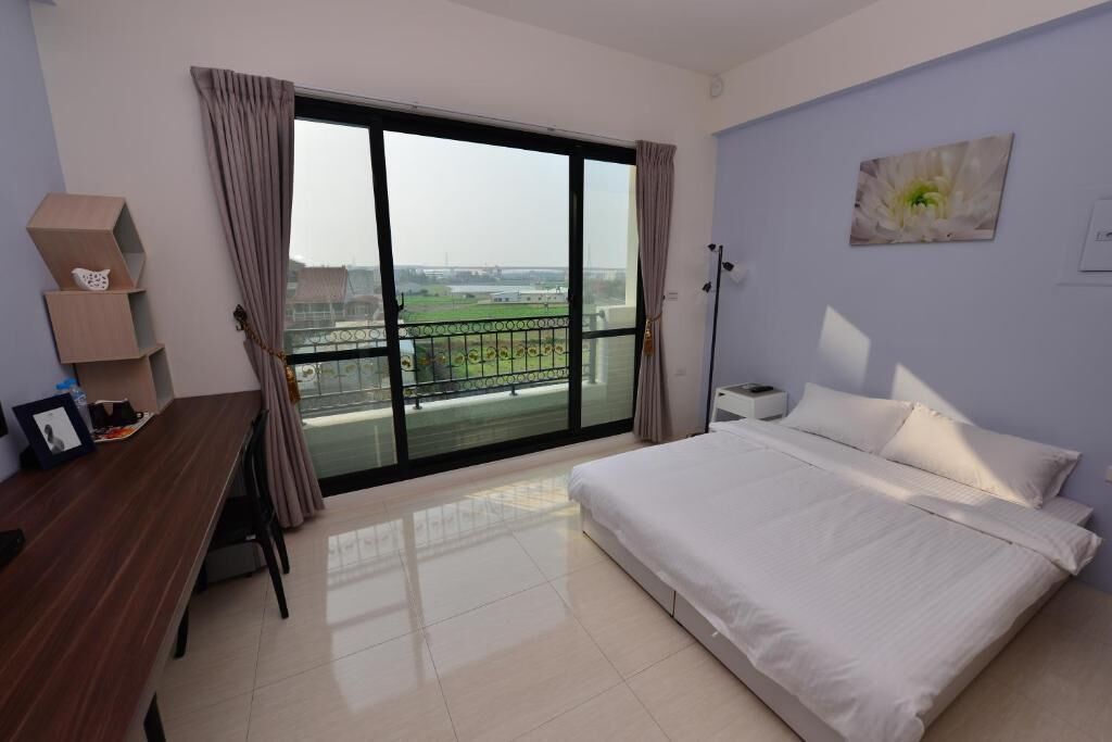 Quarto com cama grande, escrivaninha e vista para uma varanda através de uma porta de correr.