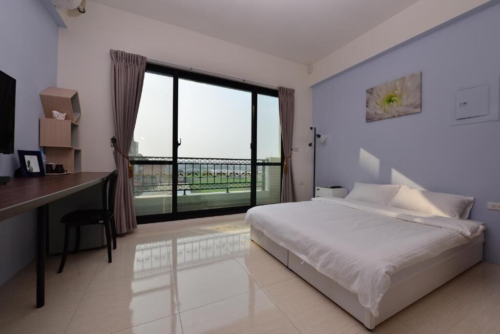 A hotel room with a bed, a desk, and a view through a large window.