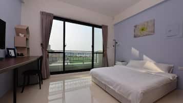 A hotel room with a bed, a desk, and a view through a large window.