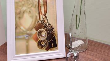 A framed photograph of a vintage camera, a clear glass vase with pink flowers, and a small silver bell on a wooden surface.