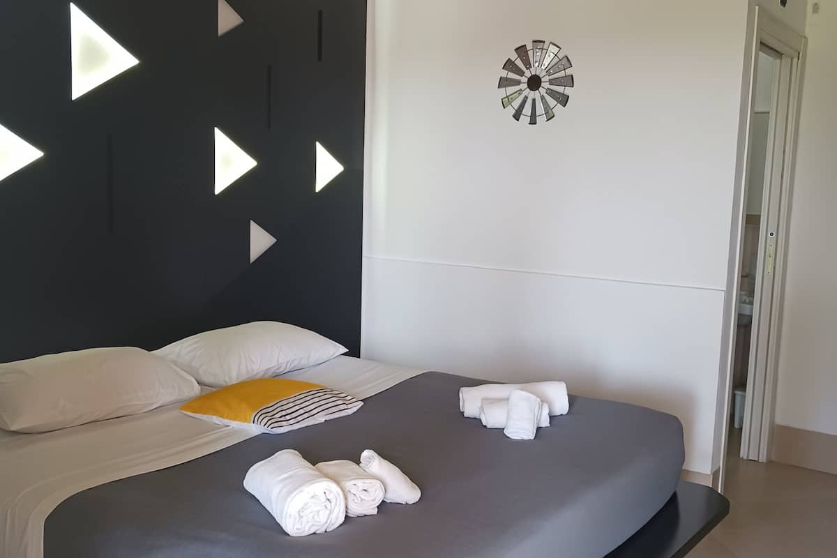 Ein modernes Hotelzimmer mit Bett, Kissen, Nachttisch, Wanduhr und Klimaanlage.