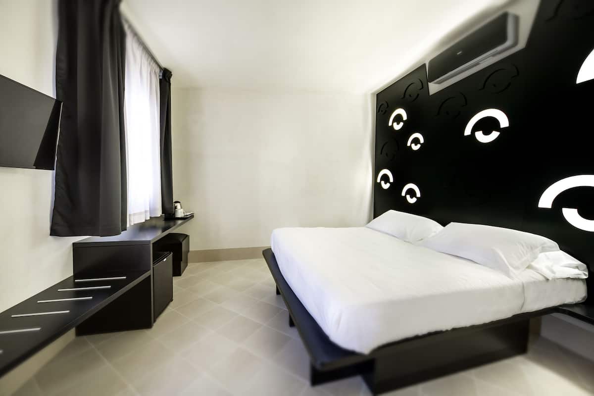Ein modernes Schlafzimmer mit Bett, Nachttischen, Schreibtisch und großem, an der Wand befestigten Fernseher.
