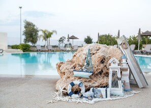 Uma área de piscina com espreguiçadeiras, uma estrutura rochosa com rede de pesca e um pequeno modelo de farol.