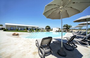 A pool area with lounge chairs and umbrellas, a clear blue sky, and a building in the background.
