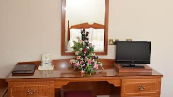 A wooden desk with a mirror, a laptop, a vase of flowers, and a red carpet.