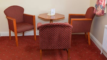 Une pièce comprenant deux fauteuils et une petite table, un tapis à motifs et un mur sur lequel est accroché un vêtement.