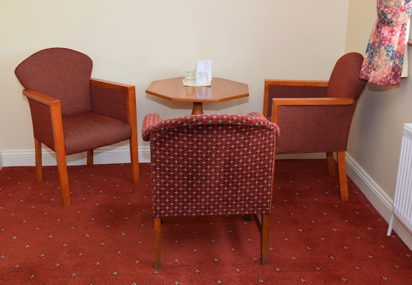 Una habitación con dos sillones, una mesita y una alfombra estampada, y una pared con una prenda colgada.