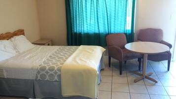 Una habitación de hotel con cama, una mesita, dos sillas y un ventanal con cortinas.