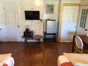 Una sala de estar con un televisor de pantalla plana montado en la pared, una cafetera y un refrigerador sobre una mesa de madera.