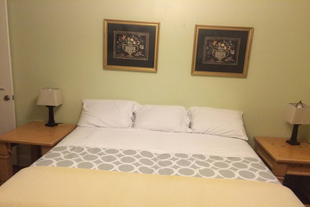 A hotel room with a bed, two nightstands, two lamps, and two framed floral paintings on the wall.