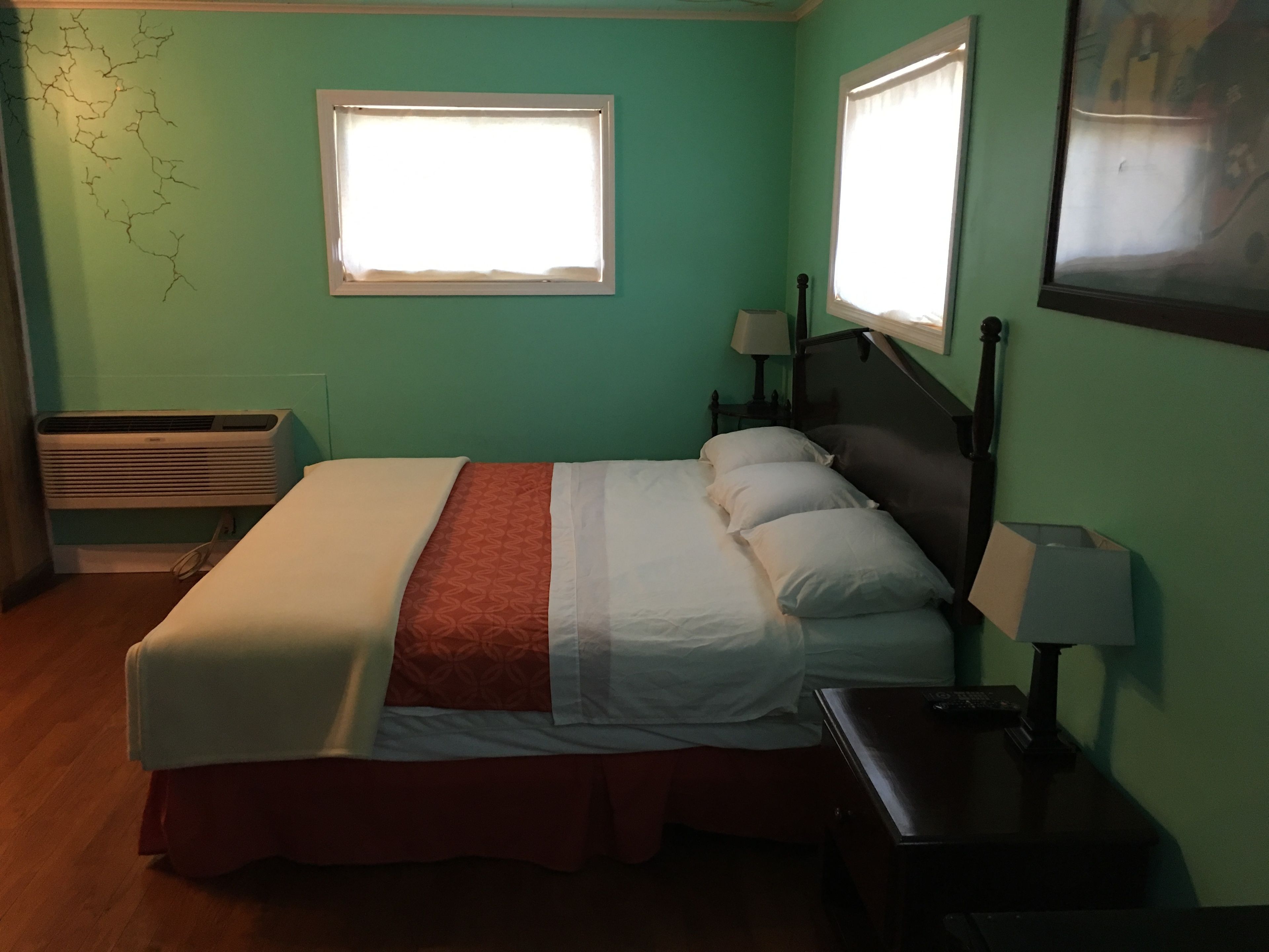A room with a bed, a window, a nightstand, and a wall-mounted air conditioner.