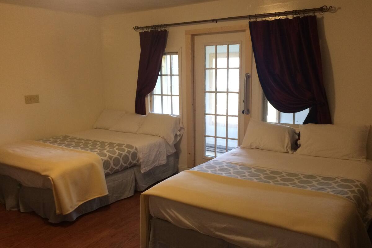 Two single beds with patterned bedding, a wooden floor, and a window with curtains.