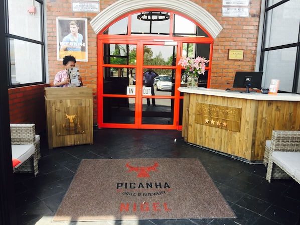 A restaurant entrance with a red archway, a wooden reception desk, and a doormat with the restaurant's name. - Picanha Grill Guest House & Events Venue (Nigel)