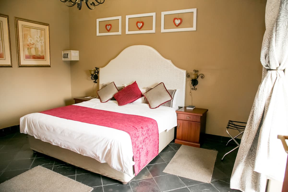 A neatly made bed with a white and red bedspread, a wooden nightstand with a lamp, and a wall with framed heart decorations.