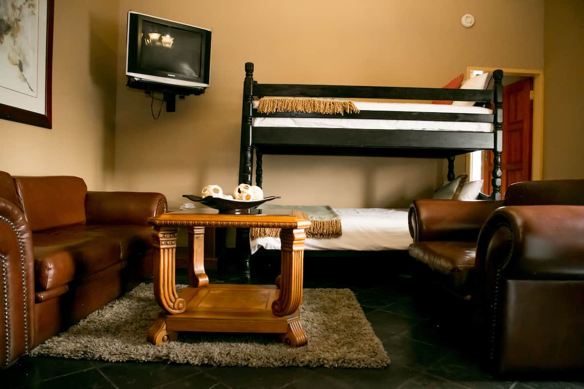 A room with a bunk bed, leather sofas, a small wooden table, a television, and a framed picture on the wall.