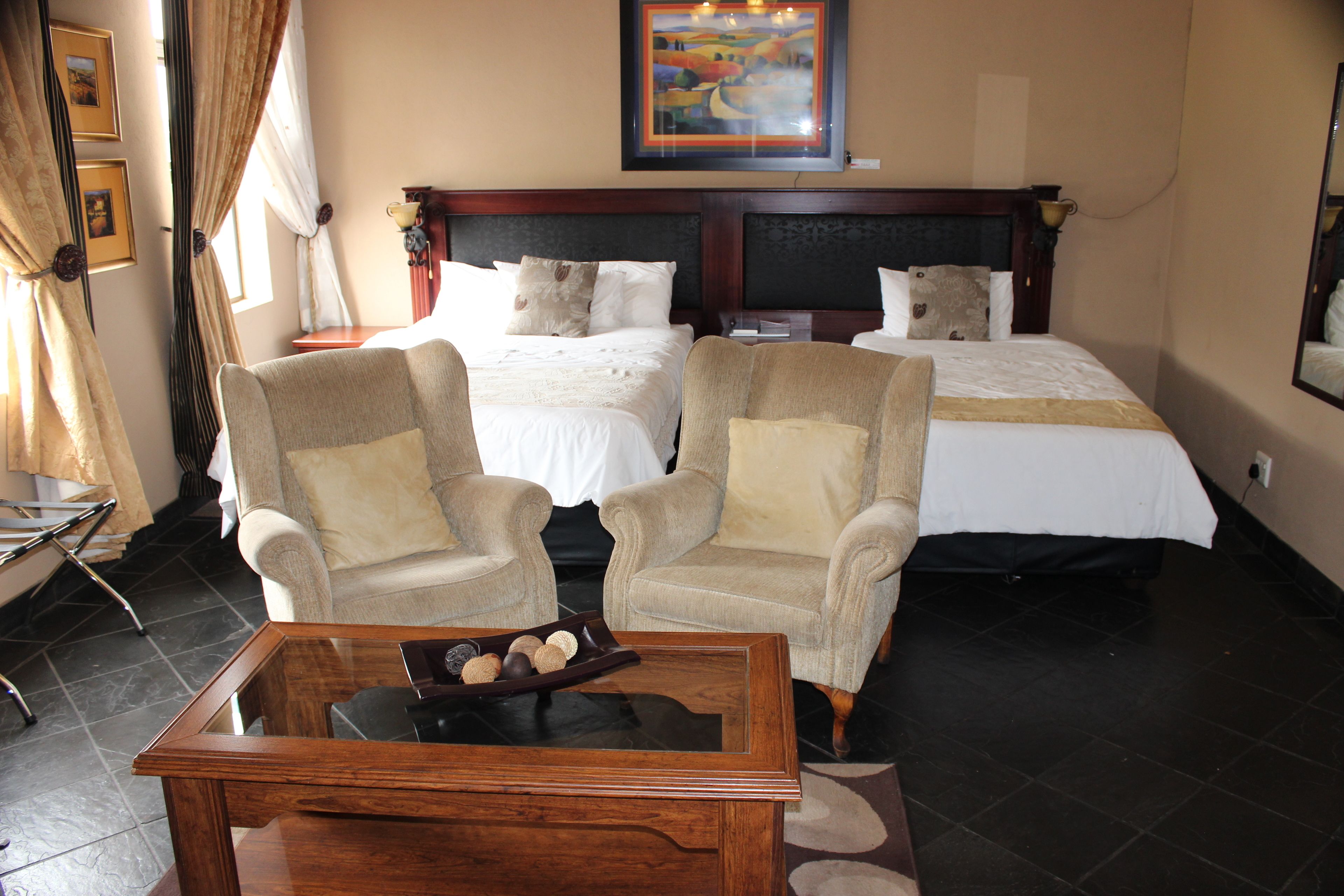 A hotel room with two beds, two armchairs, a wooden coffee table, and a painting on the wall.