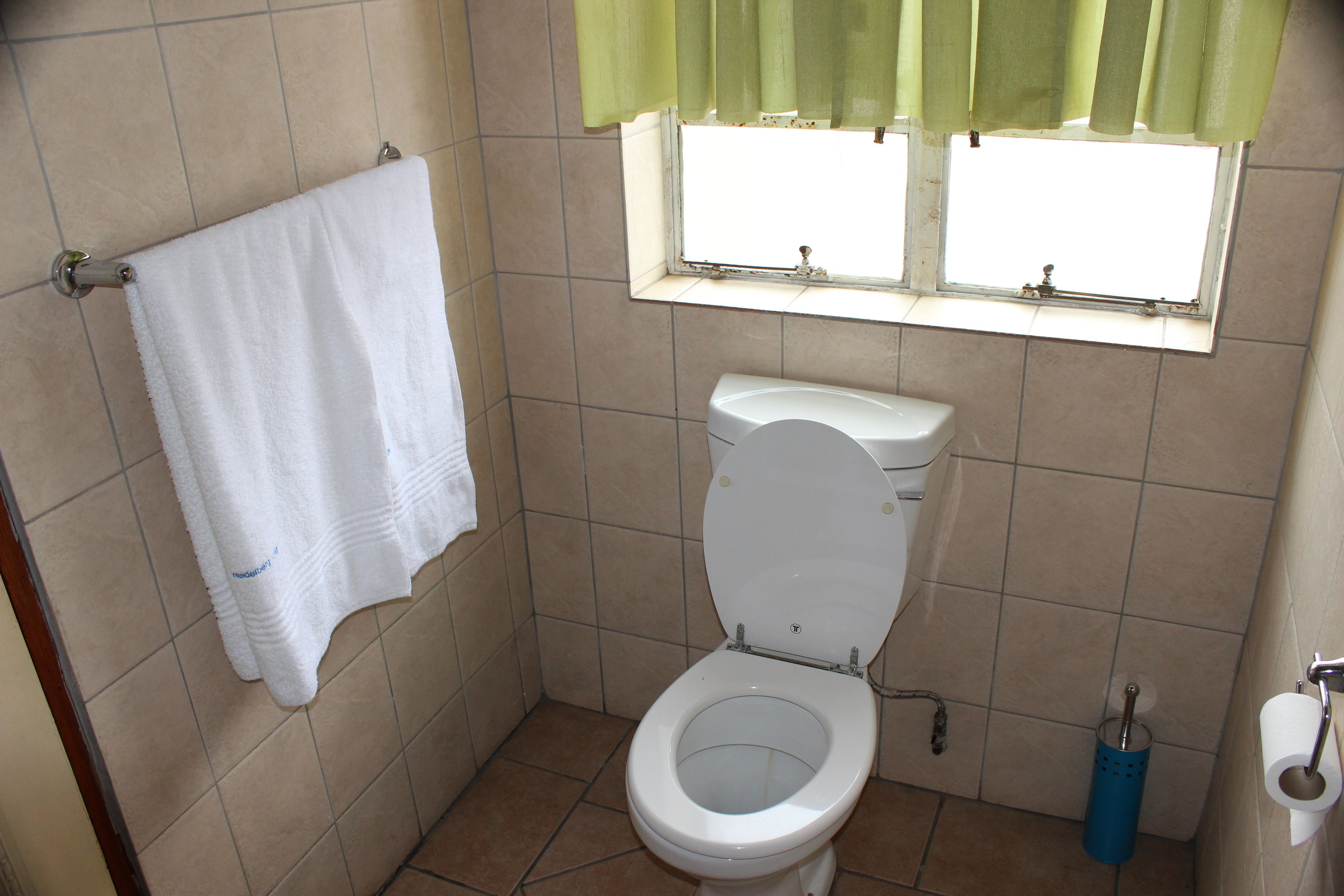 Un baño pequeño con un inodoro, una toalla colgada en un perchero y una ventana con cortinas.