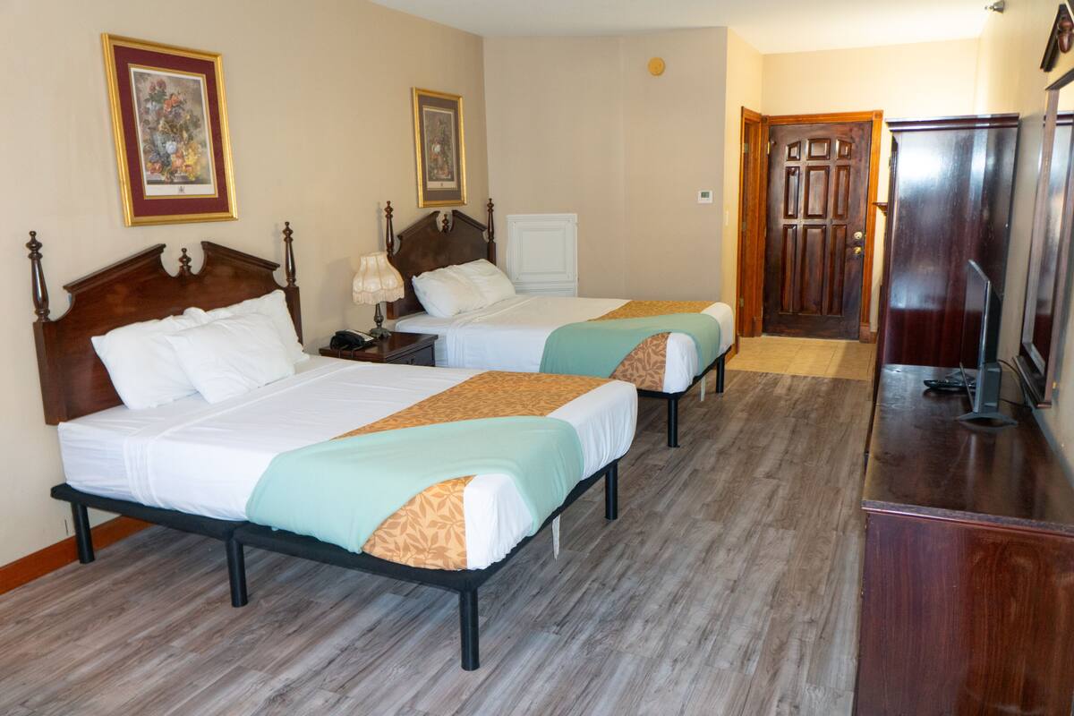 A hotel room with two beds, a wooden dresser, and a door leading to another room.