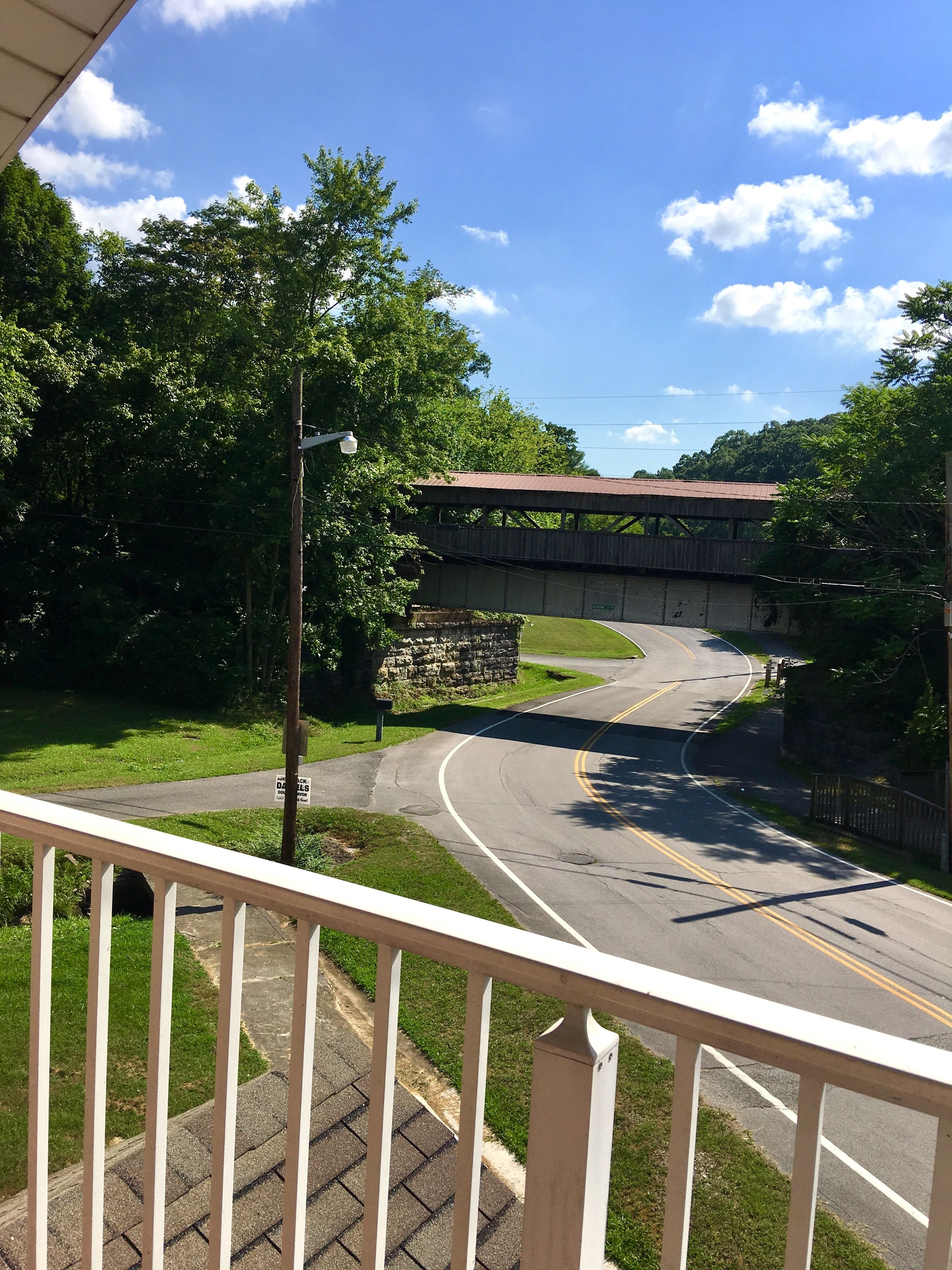 A road curving under a bridge with a stone wall and greenery on the sides.
