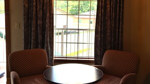 Um quarto com uma mesa redonda e duas cadeiras estampadas, um candelabro e uma janela com cortinas.