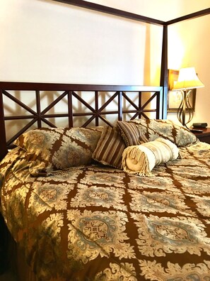A bed with a patterned bedspread and multiple pillows, a wooden headboard, and a bedside table with a lamp and remote control. - Cumberland Gap Inn (Cumberland Gap)