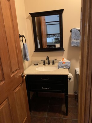 A bathroom with a wooden door, a white sink, a dark vanity, a mirror, and a towel rack. - Cumberland Gap Inn (Cumberland Gap)