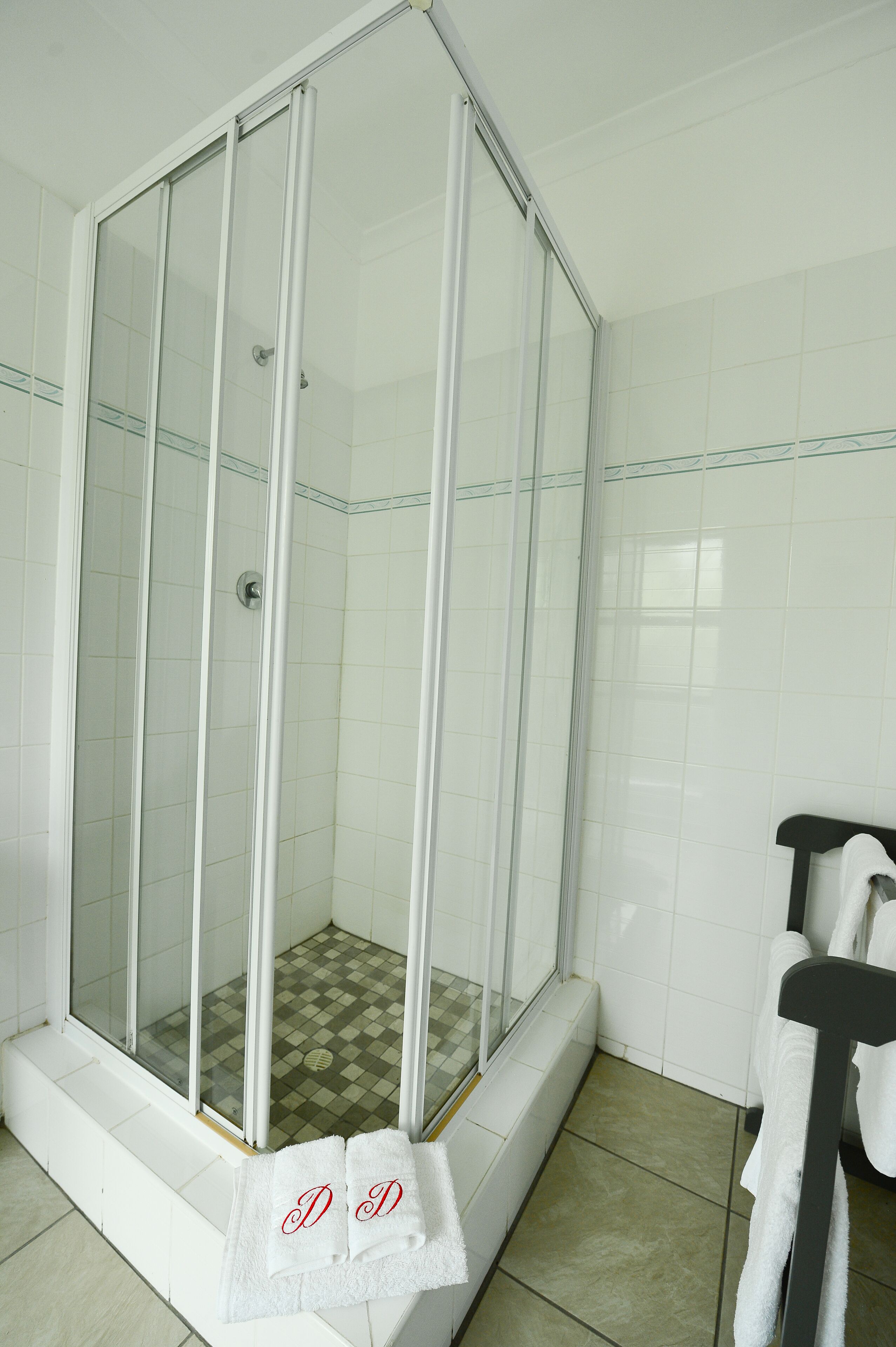 A shower area with a glass door, white tiled walls, and a checkered shower floor.